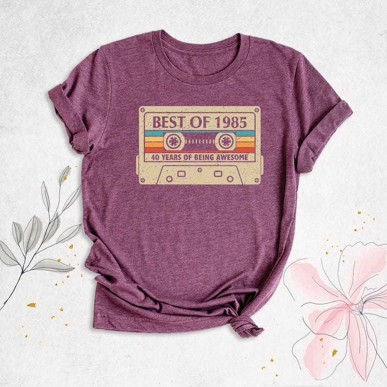 K&ouml;nnte beinhalten: Lilafarbenes T-Shirt mit einem Vintage-Kassettenband-Motiv, auf dem "Best of 1985, 40 Years of Being Awesome" steht.