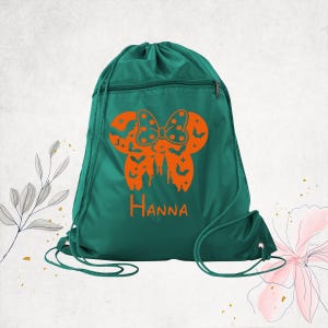 Pu&ograve; includere: Uno zaino con coulisse verde scuro con una grafica arancione di una silhouette di orecchie di topo con un fiocco a pois, un castello e pipistrelli. Il nome Hanna &egrave; stampato in arancione sotto la grafica. La borsa ha una tasca frontale.