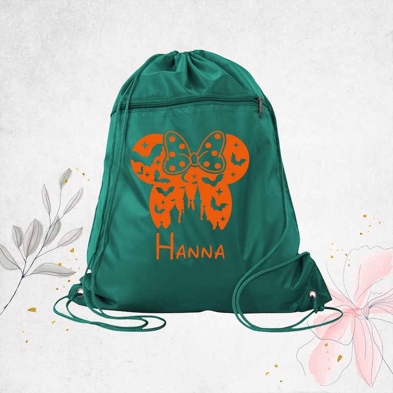 Pu&ograve; includere: Uno zaino con coulisse verde scuro con una grafica arancione di una silhouette di orecchie di topo con un fiocco a pois, un castello e pipistrelli. Il nome Hanna &egrave; stampato in arancione sotto la grafica. La borsa ha una tasca frontale.