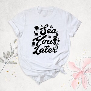 Peut inclure: T-shirt blanc avec un motif noir qui dit "Sea You Later" avec des illustrations de la vie marine.