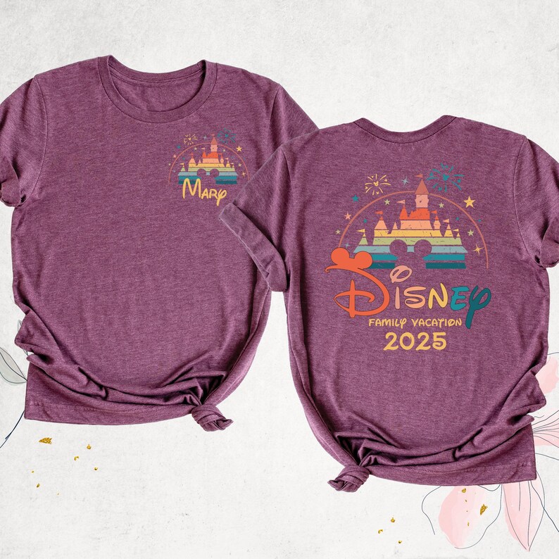 K&ouml;nnte beinhalten: Zwei lila T-Shirts mit einer regenbogenfarbenen Grafik von Schloss Aschenputtel. Das vordere Shirt sagt "Mary" und das hintere Shirt sagt "Disney Family Vacation 2025".