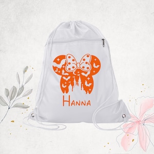 Pu&ograve; includere: Uno zaino a sacca bianco con una grafica arancione raffigurante una silhouette di orecchie di topo con un fiocco a pois, pipistrelli, stelle e un castello. Il nome Hanna &egrave; stampato in arancione sotto la grafica. Include una tasca con cerniera.
