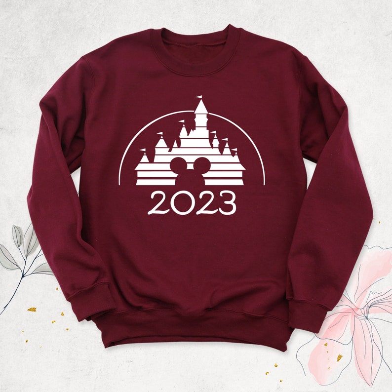May include: Burgundy sweatshirt with a white graphic of the Disney castle, Mickey Mouse ears, and the year 2023.