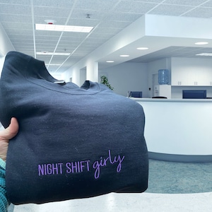 May include: A dark blue sweatshirt with the text "NIGHT SHIFT girly" embroidered in purple.