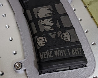 May include: A black magazine with a gray and black image of a person in a prison cell with the text "HERE WHY I AM?" printed on it.