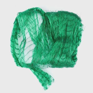 Puede incluir: Una red de malla verde brillante, probablemente para productos o almacenamiento. La red está densamente tejida, con un patrón visible de líneas que se cruzan. La forma general es irregular, lo que sugiere que ha sido recogida o atada.