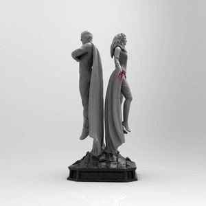 Op de afbeelding: Een grijs en wit beeld van twee figuren die op een zwarte basis staan. De figuren dragen mantels en zijn dramatisch geposeerd. Het beeld is een verzamelstuk.