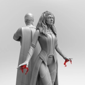Op de afbeelding: Een grijs en wit beeldje van een vrouw met lang haar en een vloeiende cape. Ze houdt een rood voorwerp in haar rechterhand. Het beeldje staat naast een grijs en wit beeldje van een man met een cape.