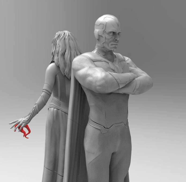Op de afbeelding: Een grijs beeldje van een superheldenpaar. De mannelijke figuur staat met gekruiste armen, terwijl de vrouwelijke figuur met haar armen langs haar zijde staat. De mannelijke figuur heeft een rode helm en een cape.