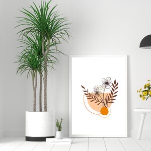 May include: A framed art print featuring a minimalist floral design in shades of brown, orange, and white. The artwork includes stylized flowers, leaves, and geometric shapes. The print is displayed on a white wall next to a potted plant.