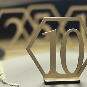 May include: A wooden table number with the number 10 in a hexagonal frame. The table number is on a brown surface.