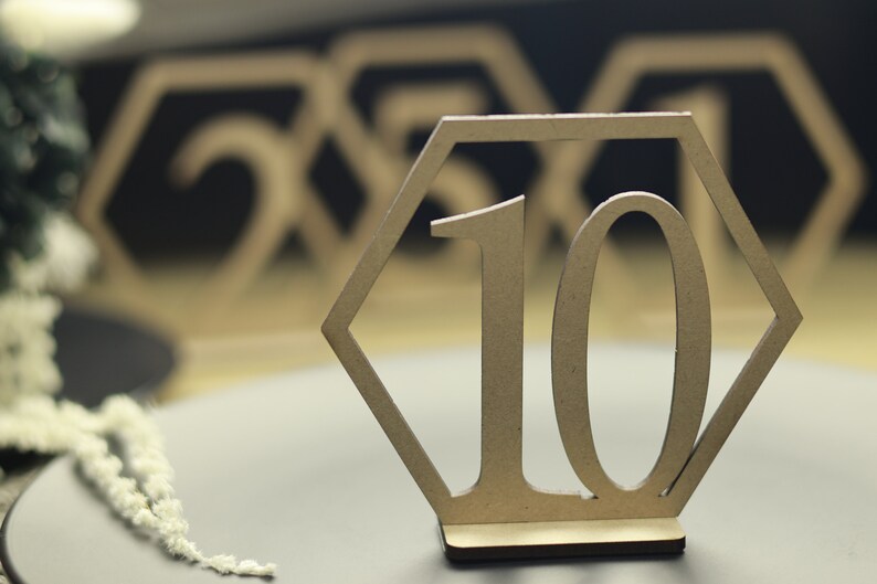 May include: A wooden table number with the number 10 in a hexagonal frame. The table number is on a brown surface.