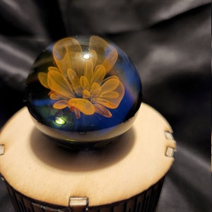 May include: A glass marble with a swirling orange and blue design. The marble is sitting on a wooden base.