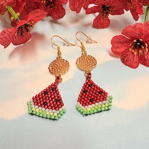 Peut inclure: Une paire de boucles d'oreilles faites à la main avec un motif de tranche de pastèque. Les boucles d'oreilles ont des accents métalliques dorés et sont faites de perles rouges, noires, vertes et blanches. Un accessoire amusant et coloré.