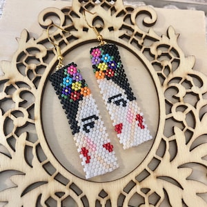 Peut inclure: Boucles d'oreilles perlées faites à la main avec un motif de portrait. Les boucles d'oreilles représentent un visage de femme avec des cheveux noirs, une couronne florale et des lèvres rouges. Les boucles d'oreilles rectangulaires ont des crochets dorés.