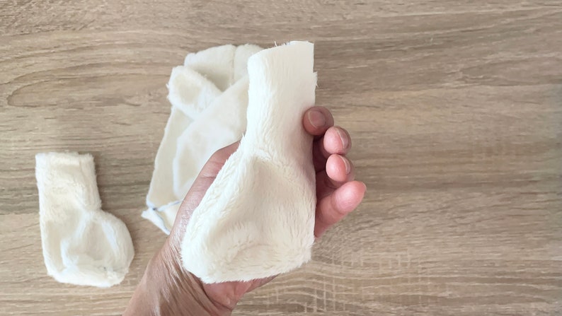 May include: White faux fur fabric pieces for sewing a plush toy. The fabric is cut into different shapes, including a long tube and two smaller pieces.
