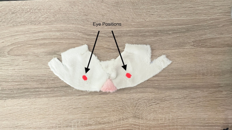 May include: White fabric with two red dots marked "Eye Positions" for placement of eyes on a plush toy.