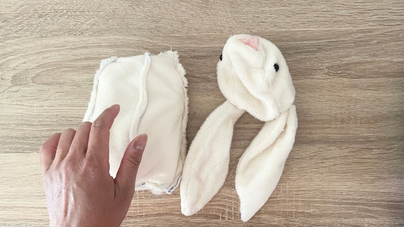 May include: A white plush bunny head with long ears and black eyes. A white fabric rectangle with a seam down the middle is also shown.