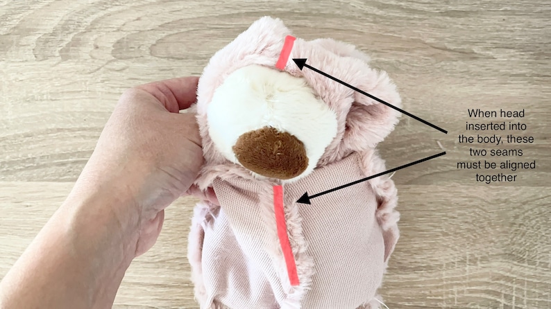 May include: Pink plush toy head with a brown nose and white fur. Two pink seams are marked with red tape. The text reads "When head inserted into the body, these two seams must be aligned together."