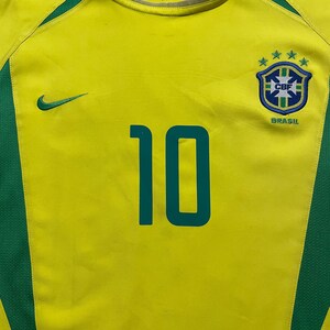 Puede incluir: Camiseta de f&uacute;tbol de Brasil amarilla y verde con el n&uacute;mero 10 en verde azulado. Presenta el logo de Nike y el escudo de la selecci&oacute;n brasile&ntilde;a. La camiseta tiene detalles verdes en hombros y laterales.