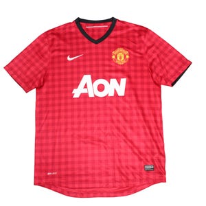 May include: Red and black checked football shirt with a V-neck collar and short sleeves. The shirt displays the Nike logo, the word "AON" in white, and a team crest. The shirt is made of Dri-FIT material.
