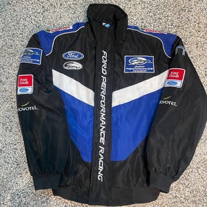 Puede incluir: Chaqueta Ford Performance Racing negra, azul y blanca. La chaqueta presenta el logotipo de Ford, logotipos de patrocinadores y la inscripción vertical "FORD PERFORMANCE RACING". Tiene cuello alto y puños y dobladillo acanalados.