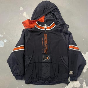 May include: Black and orange Flyers Starter jacket with a hood. The jacket has a zipper closure and the word "FLYERS" printed vertically in orange. The sleeves have orange and white stripes. The Starter logo is on the sleeve.