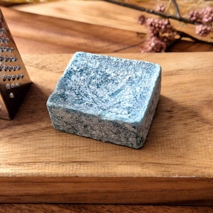 Könnte beinhalten: Eine kleine, quadratische, blaugrüne Seifenschale mit einer rauen, strukturierten Oberfläche. Die Schale ist aus einem natürlichen Material gefertigt und hat einen rustikalen Look.