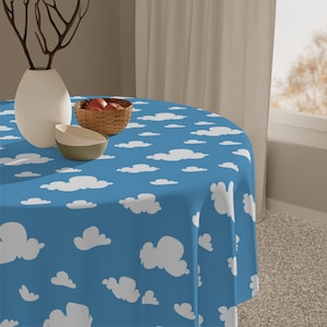 May include: A round tablecloth with a blue background and a pattern of white clouds. The tablecloth is on a round table. A white vase, a small basket, and two bowls are on the table.