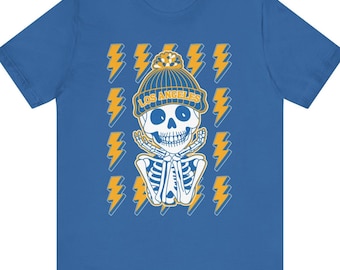Puede incluir: Camiseta azul con un esqueleto que lleva un gorro con el texto "LOS ANGELES". El diseño incluye rayos amarillos y blancos.