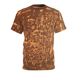 Puede incluir: Una camiseta marrón con un patrón de petroglifos antiguos. Los petroglifos son de color marrón claro y representan varios animales y símbolos.
