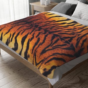 May include: A soft, plush throw blanket with a realistic tiger print in shades of orange, black, and yellow. The blanket is draped over a bed with white bedding.