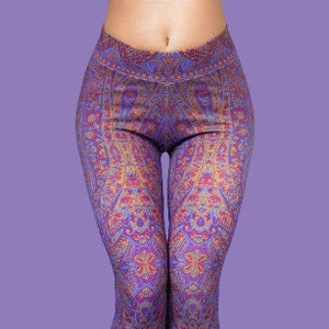 Puede incluir: Leggings moradas con un patrón intrincado y colorido. El patrón presenta una mezcla de colores naranja, rojo y azul.