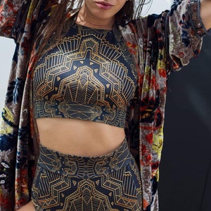 May include: A two-piece set consisting of a high-waisted bottom and a sleeveless crop top, both featuring a black fabric base with a repeating gold geometric line pattern, worn with a long, open-front velvet robe with a multi-coloured floral print.