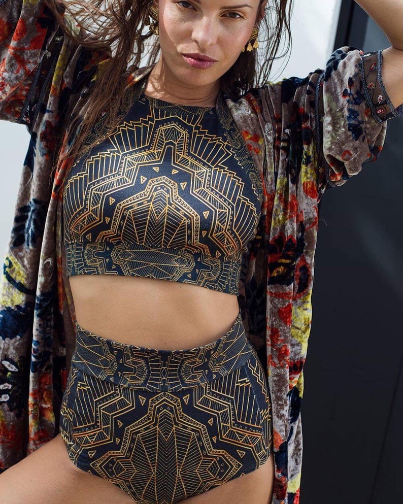 May include: A two-piece set consisting of a high-waisted bottom and a sleeveless crop top, both featuring a black fabric base with a repeating gold geometric line pattern, worn with a long, open-front velvet robe with a multi-coloured floral print.