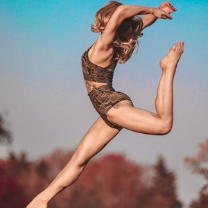 May include: A two-piece athletic set featuring a dark brown crop top and high-waisted bottoms, both adorned with a repeating geometric pattern in a lighter tan shade. The garments are form-fitting and designed for active movement and flexibility.