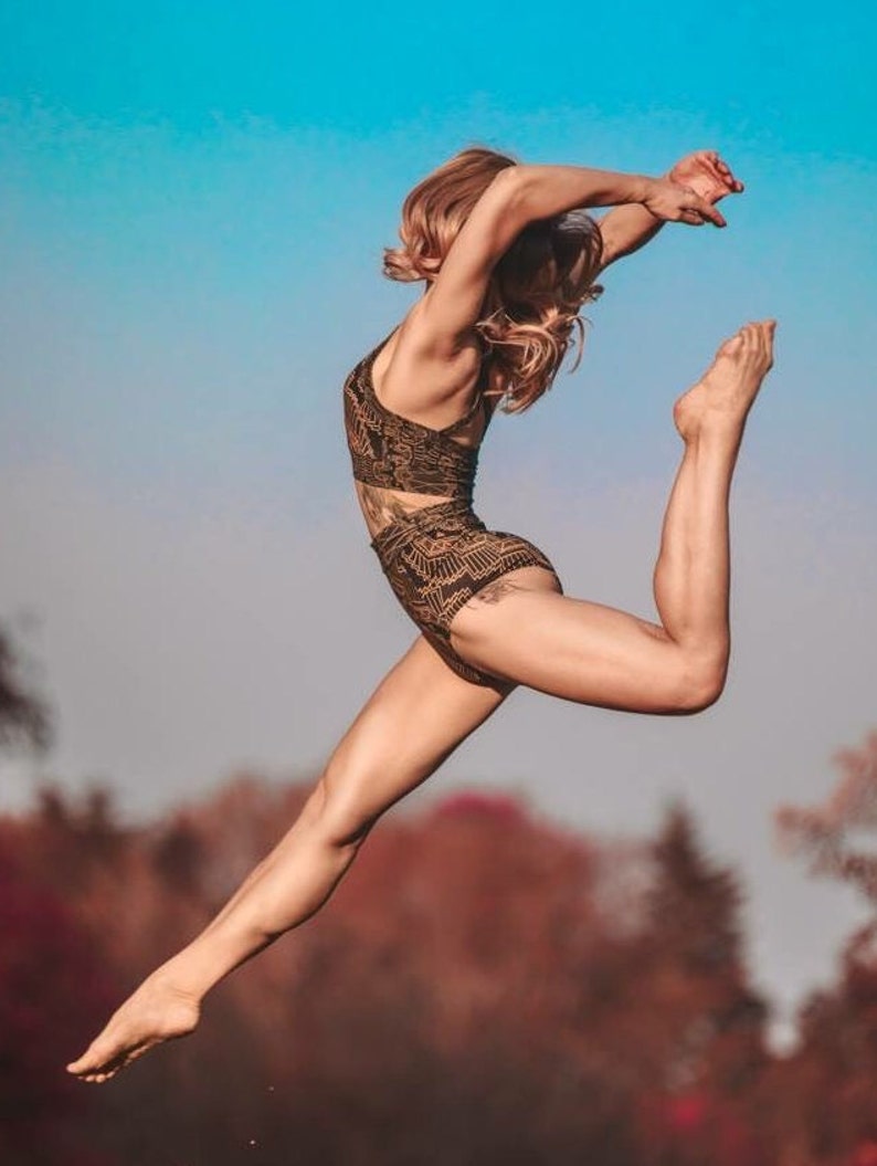 May include: A two-piece athletic set featuring a dark brown crop top and high-waisted bottoms, both adorned with a repeating geometric pattern in a lighter tan shade. The garments are form-fitting and designed for active movement and flexibility.