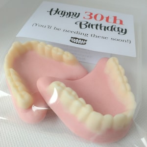 May include: A white card with the text "Happy 30th Birthday (You'll be needing these soon!)" and a small image of a set of dentures. Two pink and white dentures are in a clear plastic bag.