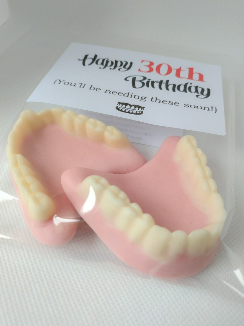 May include: A white card with the text "Happy 30th Birthday (You'll be needing these soon!)" and a small image of a set of dentures. Two pink and white dentures are in a clear plastic bag.