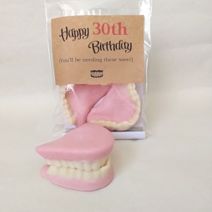 May include: A brown paper bag with a tag that reads "Happy 30th Birthday (You'll be needing these soon!)" and a small image of dentures. The bag contains a set of pink and white plastic dentures.