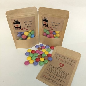 May include: Two brown paper bags with a clear window showing colourful candy inside. The bags have a red cross and the text "Anti - Late for work Pills".