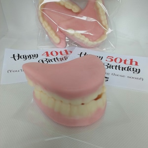 May include: Two sets of novelty plastic dentures in a clear plastic bag. The dentures are pink and white and have the text "Happy 40th Birthday" and "Happy 50th Birthday" on the cards behind them.