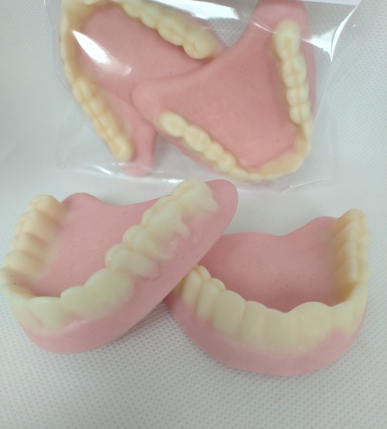 May include: A set of four pink and white gummy teeth. The teeth are shaped like dentures and are a fun and quirky treat.