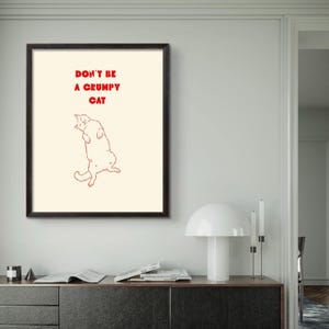 Könnte beinhalten: Gerahmter Kunstdruck mit dem roten Text "DON'T BE A GRUMPY CAT". Der Druck zeigt eine rote Umrisszeichnung einer Katze. Der Rahmen ist schwarz. Der Druck wird auf cremefarbenem Hintergrund angezeigt.