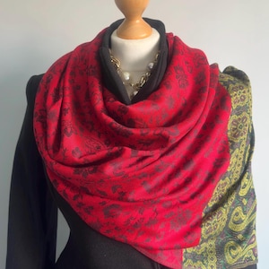 May include: A red scarf with a black floral pattern and a green and gold paisley border. The scarf is draped around a mannequin's neck.
