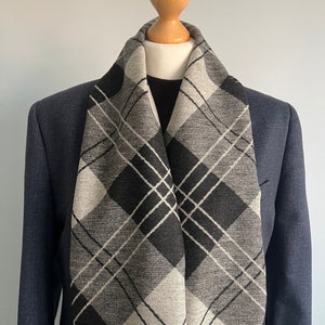 Pode incluir: Uma echarpe xadrez preta e branca com um padrão de diamante. A echarpe está drapeada sobre um manequim que veste um blazer azul marinho.