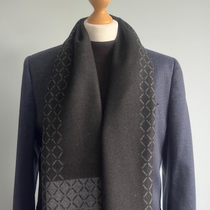 May include: A black and grey patterned scarf with a geometric design. The scarf is folded and draped over a mannequin wearing a blue blazer.