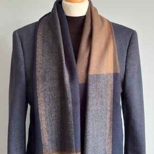 May include: A navy blue blazer with a brown scarf draped over a brown sweater. The scarf features a plaid pattern in shades of navy, brown, and tan. The items are displayed on a mannequin.
