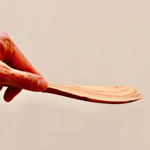 May include: A wooden spatula with a natural wood finish. The spatula is curved and has a wide, flat blade.
