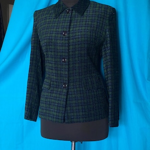 May include: A green and navy blue tweed blazer with a classic collar and button closure. The jacket has long sleeves and two small pockets. The blazer is displayed on a black mannequin.